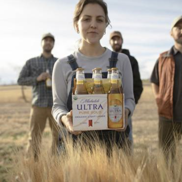 woman in a field carrying a 6 pack of Michelob beer