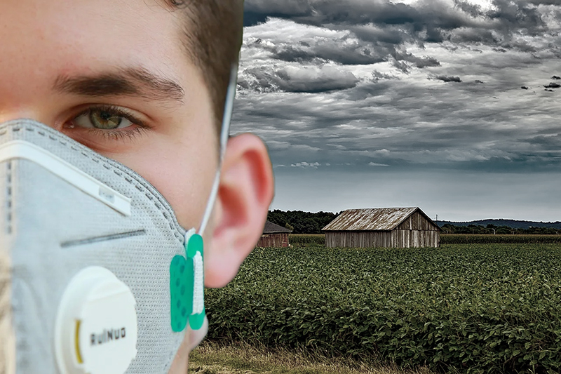 man in a face mask standing in front of a farm field