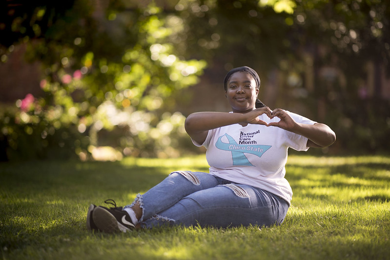 A PATH scholars student sitting in the grass, holding up a heart with her hands.