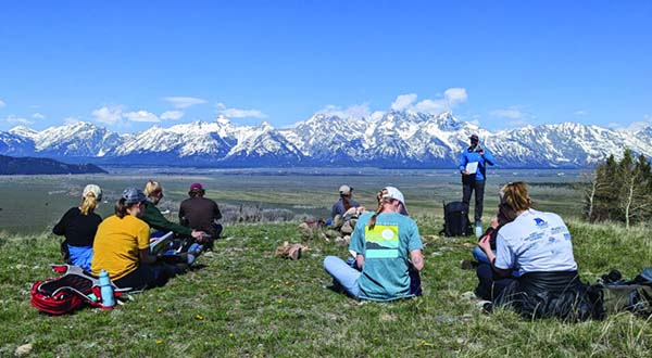 Students sitting on grass facing mountains