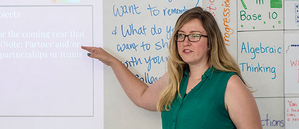 Woman at front of class explaining something on white board