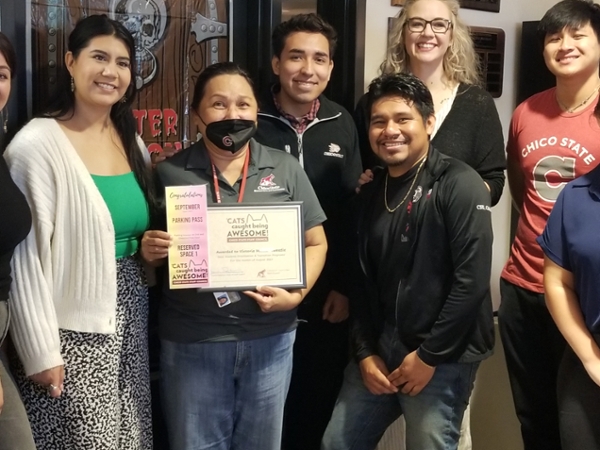 Victoria holds certificate and parking pass while surrounded by colleagues