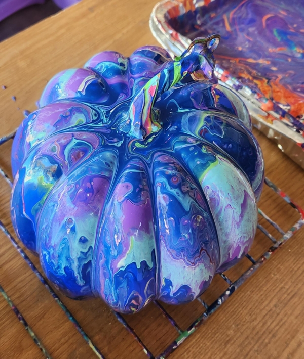 A pumpkin entirely covered in marbled blue, purple, and green paint, including the stem.