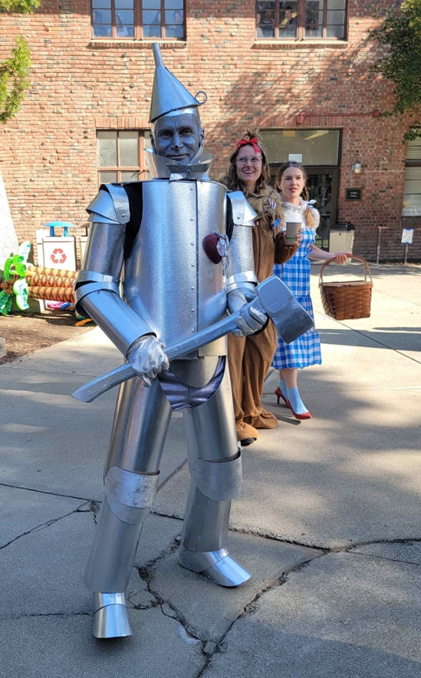 David Barta standing outside Ayers Hall dressed in a beautiful  handmade costume of the Tin Man from the Wizard of Oz. His face is painted silver, he carries a fake silver ax, and he has a heart medal stuck to the breast of his suit.