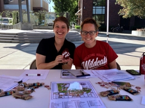 Kate Post and Ashley Gebb sitting behind volunteer Ask Me! table on Chico State campus.