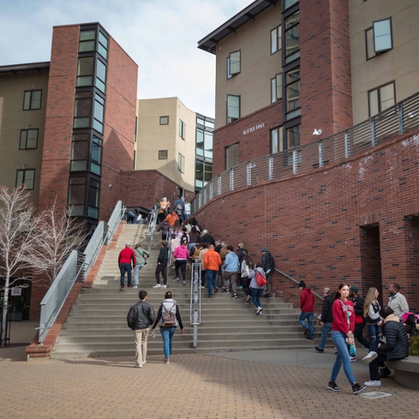 Students walk along the footpath and staircase outside of Éstom Jámani Hall (formerly Sutter Hall at sunset.)