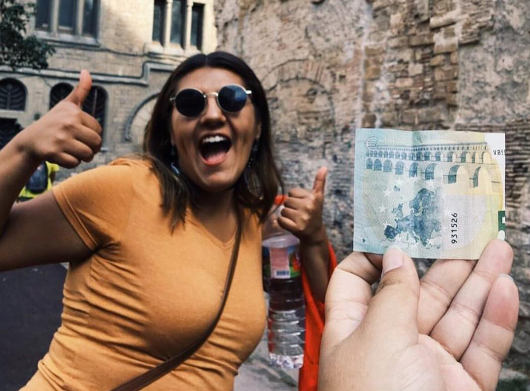 Picture of a person with their thumbs up and a 5 euro note in the foreground