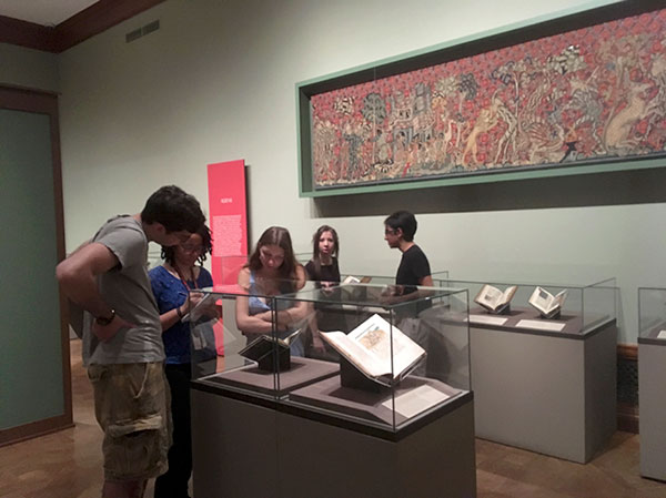 group of students examining contents of glass case with artwork on the wall in the background