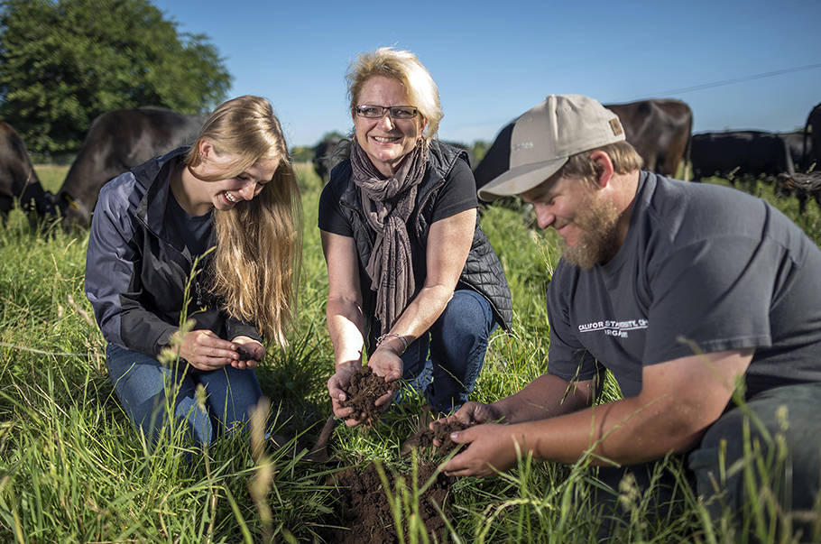 Cindy Daley with students examining soil with cows in the field