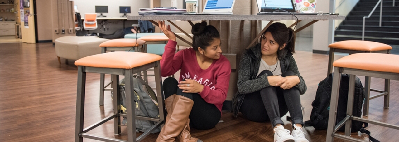 Two students practice earthquake safety by crouching under a table