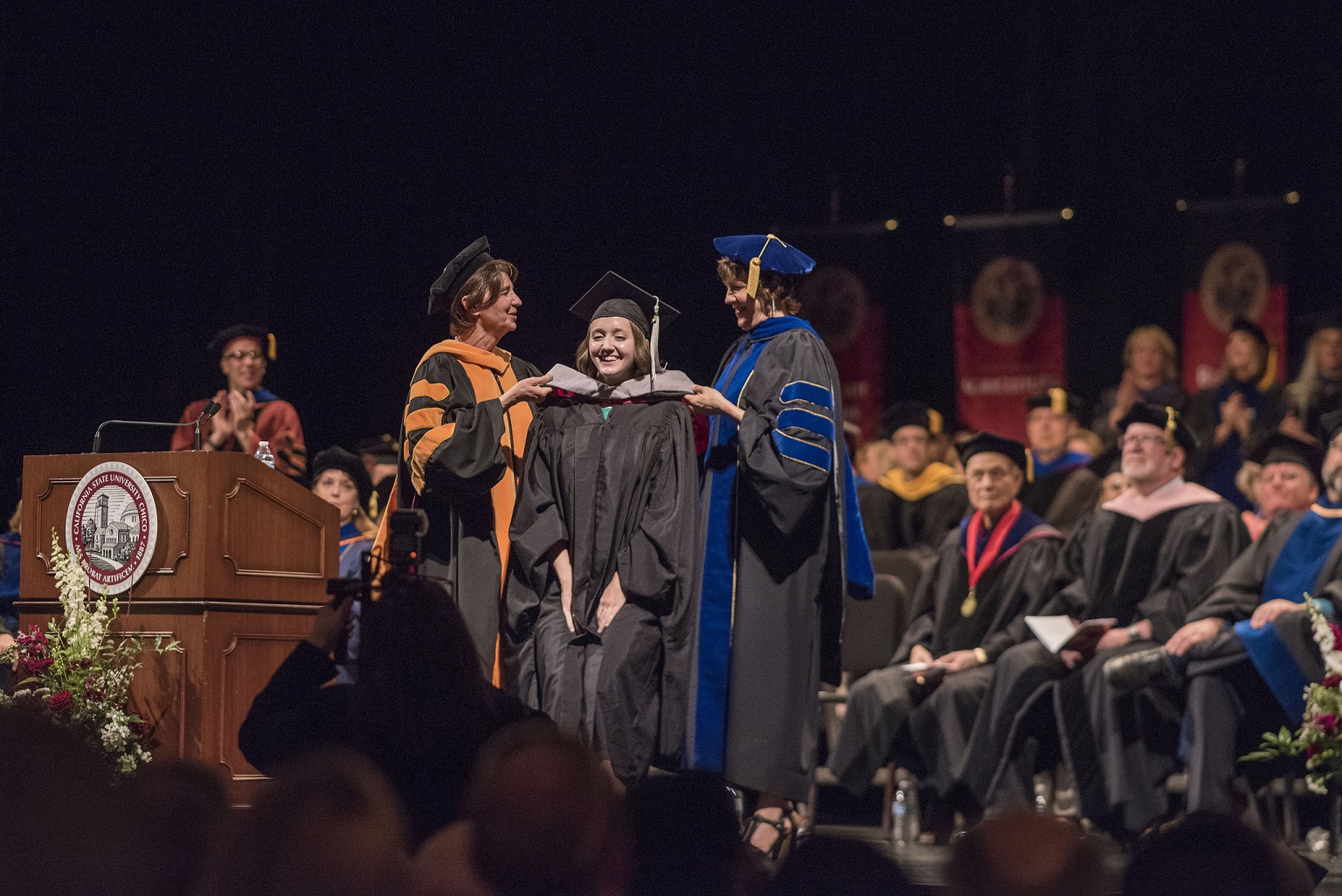 Provost Debra Larson (left) and Angela Trethewey (Dean, CME) (right) hood graduate students in Communication And Education (CME) at the Master's Commencement Ceremony